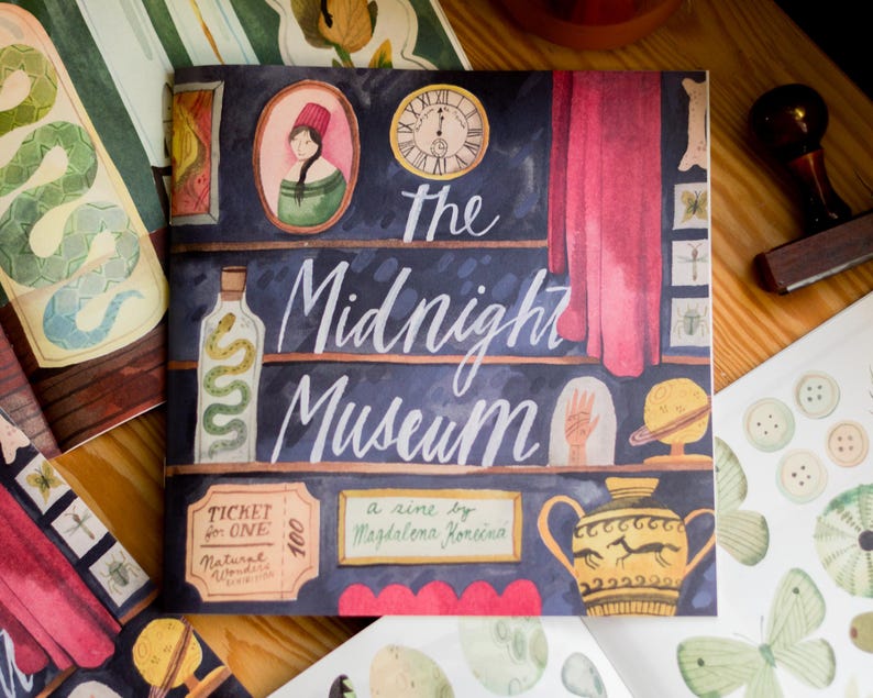 May include: The Midnight Museum, a zine by Magdalena Fonseca, illustrated with a watercolor style. The cover features a dark blue background with shelves filled with various objects, including a bottle with a snake inside, a clock, a hand, a globe, and a vase with a horse design. The title "The Midnight Museum" is written in white cursive lettering.
