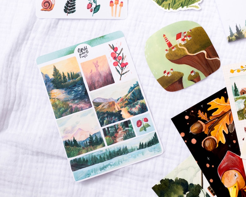 May include: A sheet of stickers featuring watercolor illustrations of nature scenes. The stickers include a deer in a forest, a mountain range, a lake, and a forest path. The stickers are printed on white paper and have a matte finish.