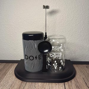 May include: A black and white coffee set with the word "DOSE" on a cylindrical container with a wavy pattern. A clear glass with the words "EVERYDAY DOSE" and mushroom graphics. A black spoon and frother are also included.