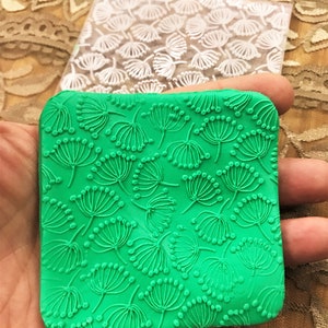 May include: Green silicone baking mat with a raised design of small white flowers. The mat is square shaped and has a textured surface.