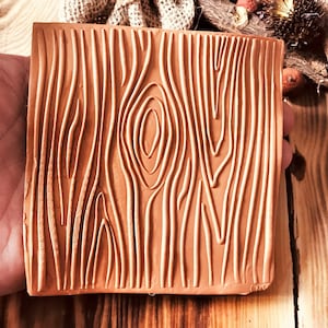 Könnte beinhalten: Ein brauner Gummistempel mit Holzmaserung. Der Stempel ist etwa 7,6 cm x 7,6 cm groß.