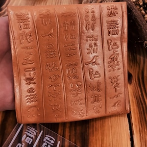May include: A rectangular terracotta tile with raised hieroglyphic symbols in a brown color. The tile is decorated with images of birds, water, and other symbols.
