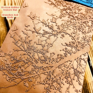 Könnte beinhalten: Eine 10-14 cm große Gummimatte mit einer Textur, die Äste und Vögel darstellt. Die Matte ist braun und hat eine strukturierte Oberfläche.