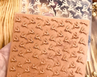 Könnte beinhalten: Ein brauner Silikonstempel mit einem sich wiederholenden Muster von laufenden Rentieren. Der Stempel liegt auf einer transparenten Plastikfolie mit dem gleichen Muster.