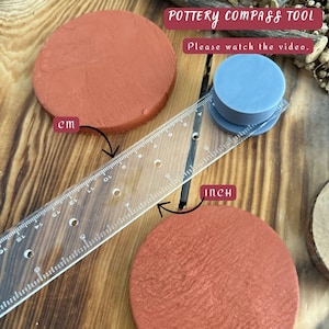 May include: A pottery compass tool with a clear ruler, two terracotta-coloured clay circles, and a blue plastic tool. The ruler is marked in inches and centimetres. The text "POTTERY COMPASS TOOL" and "Please watch the video" are visible.