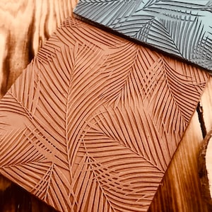 May include: Two textured rubber stamps with a palm leaf design. The top stamp is gray and the bottom stamp is brown.