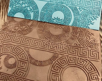 Könnte beinhalten: Zwei braune und blaue Gummistempel mit einem sich wiederholenden Muster aus Kreisen mit einem griechischen Schlüsselmuster. Die Stempel befinden sich auf einer Holzoberfläche.