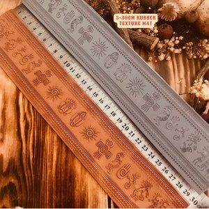 May include: Two 5-30cm rubber texture mats with a repeating pattern of geometric shapes and symbols. The mats are laid out side-by-side on a wooden surface. The mats are gray and brown.