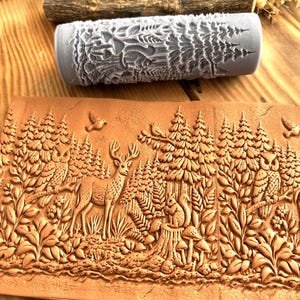 May include: A gray, textured rolling pin with a forest design sits above a brown, embossed leather piece depicting a forest scene with a deer, owl, and squirrel. The leather piece is detailed with trees, plants, and birds.