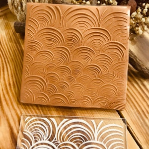 May include: A brown rubber stamp with a raised design of overlapping circles. The stamp is used to create a decorative pattern on paper or other surfaces.