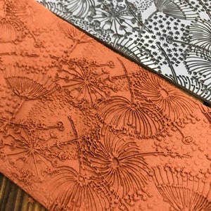 May include: A close-up of a textured, orange-brown rubber stamp with a design of stylised flowers. The stamp is made of a soft, flexible material and has a raised design.