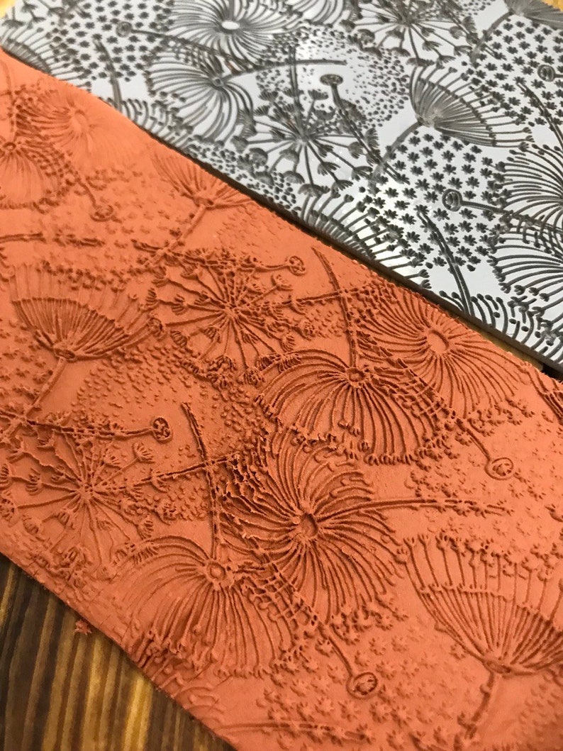 May include: A close-up of a red clay stamp with a detailed design of a flower with many petals. The stamp is used to create a raised design on paper or fabric.