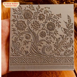 May include: A 10-10cm rubber texture mat with a detailed floral design. The mat features a repeating pattern of leaves, flowers, and swirls. The design is embossed into the rubber, creating a raised texture.