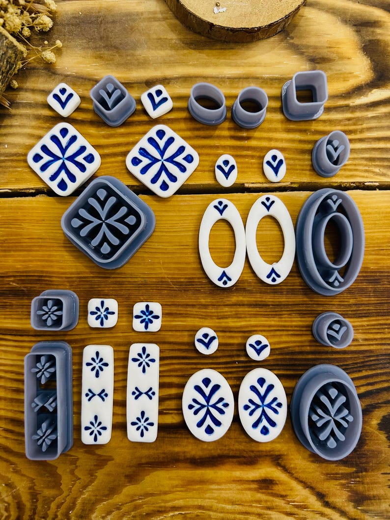 May include: A set of 20 polymer clay cutters in various shapes and sizes, including squares, ovals, and rectangles. The cutters are gray and feature a snowflake design. The set also includes several white polymer clay pieces with blue snowflake designs.
