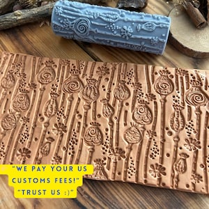 May include: A light blue patterned rolling pin and a brown embossed leather piece with a floral design. The leather piece has a repeating pattern of flowers and seed pods. The rolling pin is cylindrical and has a floral design.
