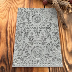 May include: A grey rubber stamp with a detailed design featuring foxes, birds, and floral patterns. The stamp is on a wooden surface.