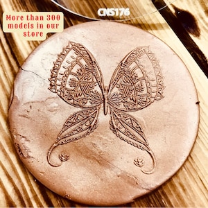 Op de afbeelding: Een ronde, terracotta kleurige onderzetter van klei met een gedetailleerd, ingewikkeld vlinderontwerp in koperkleur. De tekst "More than 3000 models in our store" is zichtbaar in de linkerbovenhoek van de afbeelding.