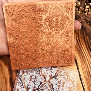 May include: Two silicone stamps featuring a damask pattern. The top stamp is brown and the bottom stamp is clear with a white design.