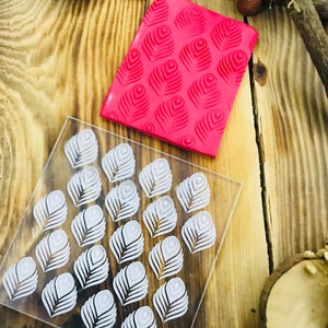 May include: A clear acrylic stamp sheet with a white design of 24 peacock feathers. A red silicone stamp with a raised design of peacock feathers is also shown.