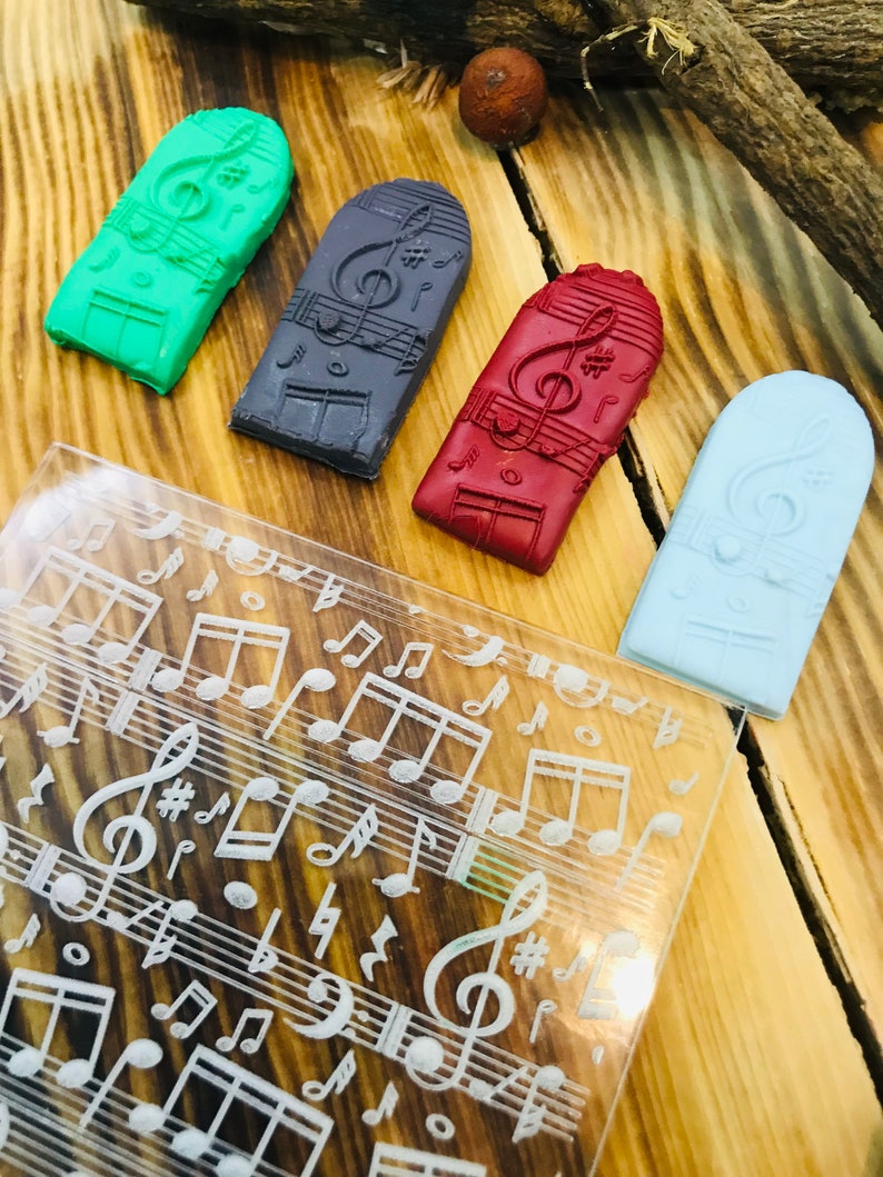 K&ouml;nnte beinhalten: Vier rechteckige, farbenfrohe Seifenst&uuml;cke mit Musikmotiven in Gr&uuml;n, Grau, Rot und Hellblau, jeweils mit einem Notenschl&uuml;ssel und Noten. Eine transparente Acrylplatte mit ge&auml;tzten Noten und Symbolen ist ebenfalls vorhanden.