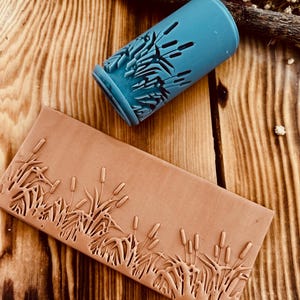 Pode incluir: Um rolo de silicone azul com um desenho em relevo de juncos. O rolo é usado para criar um padrão em relevo em argila ou fondant.