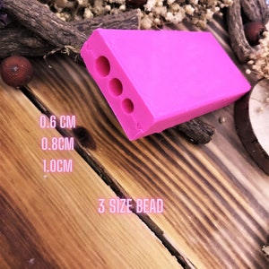May include: Pink plastic bead making tool with three holes of different sizes: 0.6 cm, 0.8 cm, and 1.0 cm.  3 Size Bead.