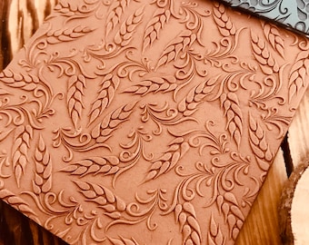 May include: Two brown and gray textured rolling pins with a wheat and floral design. The rolling pins are on a wooden surface.