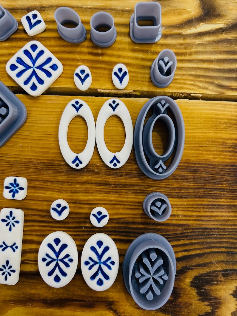 May include: A set of 18 cookie cutters in various shapes and sizes, including circles, ovals, squares, and a snowflake design. The cutters are made of a light gray plastic and are arranged on a wooden surface.