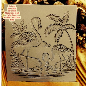 Op de afbeelding: Een rubberen stempel met een ontwerp van twee flamingo's en een palmboom. De stempel is 7-7cm, 10-10cm, 14-14cm groot. De tekst "Flamingo And Palm Trees Rubber Texture Mat" is op de stempel gedrukt.