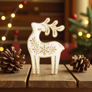 May include: A white and gold decorative reindeer figurine with intricate floral and snowflake designs. The reindeer is standing on a wooden surface, with pine cones and Christmas lights in the background. A festive holiday decoration.