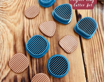 Può includere: Un set di cinque tagliabiscotti in argilla polimerica blu con disegni a strisce. I tagliabiscotti sono disposti su una superficie di legno con campioni di argilla marrone.