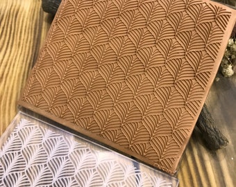 May include: Two silicone stamps with a geometric pattern of overlapping leaves. The top stamp is brown and the bottom stamp is clear with a white design.