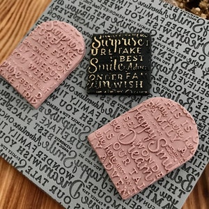 May include: Three rubber stamps with arched tops. The stamps are pink, black, and gold. The pink stamp says "Happy Dreams is our best day ever". The black stamp says "Surprise, retake best smile adventure, wonder family, on wish". The gold stamp says "Surprise, retake best smile adventure, wonder family, on wish".