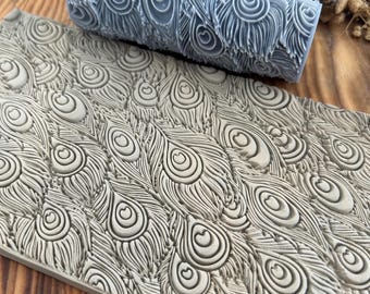 May include: A light gray textured roller and a matching rectangular tile, both featuring a peacock feather design. The roller is cylindrical, and the tile is rectangular. The design is a repeating pattern of stylized peacock feathers.