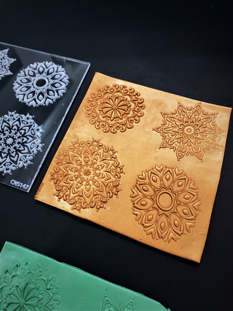 May include: A clear plastic sheet with four mandala designs, used to create impressions in leather. The sheet is labeled "CNS147".  A piece of brown leather with four embossed mandala designs is shown next to the sheet.