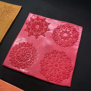 May include: Four red polymer clay stamps with intricate mandala designs. The stamps are arranged in a square pattern on a red background.
