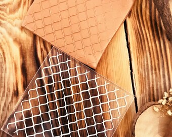 May include: Two square silicone stencils with a grid pattern. The top stencil is brown and the bottom stencil is clear with a white grid pattern. The bottom stencil has the text "CNS062" printed on it.