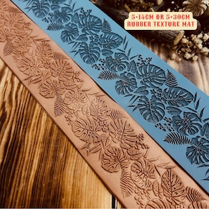 May include: Two rubber texture mats featuring a tropical leaf design. The top mat is blue and the bottom mat is brown. The mats are 5 inches wide and come in two lengths: 14 cm or 30 cm. The text "5-14CM OR 5-30CM RUBBER TEXTURE MAT" is printed on the blue mat.