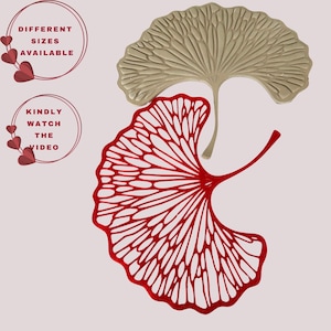 May include: Two ginkgo leaf-shaped wall decorations, one in a solid beige and one in a vibrant red with a cut-out vein pattern. Text on the left reads DIFFERENT SIZES AVAILABLE and KINDLY WATCH THE VIDEO, accented by small red heart icons.
