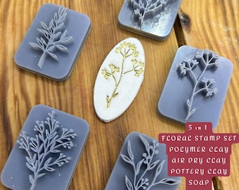 May include: A floral stamp set with five gray rectangular stamps featuring botanical designs, alongside a white oval with a gold floral design. The text "5 in 1 FLORAL STAMP SET" is visible.