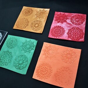 May include: Four silicone mats with different mandala designs. The mats are in gold, red, green, and orange.