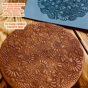 May include: A close-up of a 14 cm rubber texture mat with a floral design. The mat is brown and has a raised design. The mat is used for creating textures in clay.