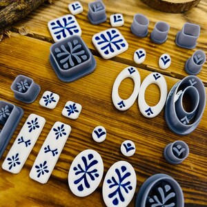 May include: A set of 18 polymer clay cutters in various shapes and sizes, including circles, ovals, squares, and rectangles. The cutters are gray and feature a white and blue geometric design.