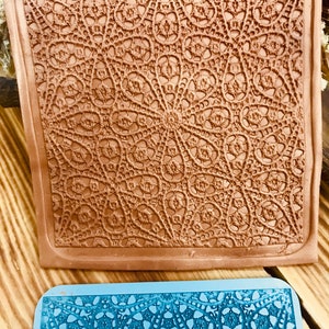 Può includere: Due tappetini da forno in silicone con un motivo a pizzo. Il tappetino superiore è marrone e quello inferiore è blu.