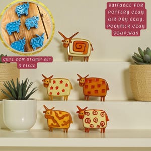 Pode incluir: Um conjunto de cinco selos decorativos em forma de vaca em vários designs e cores, incluindo azul, laranja e creme. A imagem mostra o texto "CUTE COW STAMP SET 5 PIECE" e "SUITABLE FOR POTTERY CLAY AIR DRY CLAY POLYMER CLAY SOAP.WAX."