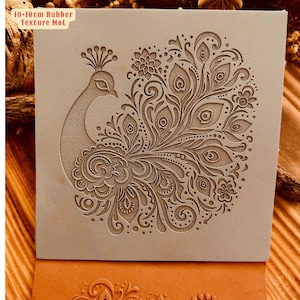 May include: A 10-inch by 10-inch rubber texture mat featuring a detailed peacock design. The mat is beige and the peacock design is brown.