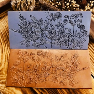 Może przedstawiać: Dwa prostokątne stemple silikonowe z wzorem kwiatowym. Górny stempel jest szary, a dolny brązowy.