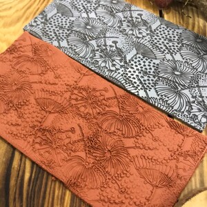 May include: Two rectangular rubber stamps with a raised design of dandelion flowers. The top stamp is grey and the bottom stamp is orange.