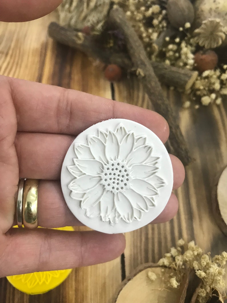 May include: White silicone mold with a raised design of a sunflower. The mold is round and has a smooth surface.