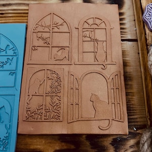 Può includere: Un timbro in gomma marrone con quattro disegni di finestre ad arco con gatti e uccelli. Ogni finestra ha un design diverso, tra cui un gatto che guarda fuori dalla finestra, un gatto seduto nella finestra e uccelli appollaiati su un ramo.